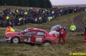 Jani Paasonen's wrecked Lancer sits in the foreground while Marcus Gronholm's 206 rests in the background, both cars crashing out at the same corner