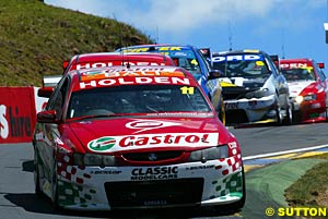 Steven Richards and Larry Perkins holds up a train of cars behind him, with Marcos Ambrose and Russell Ingall, Craig Lowndes and Glenn Seton, and Mark Skaife and Todd Kelly visible in the background